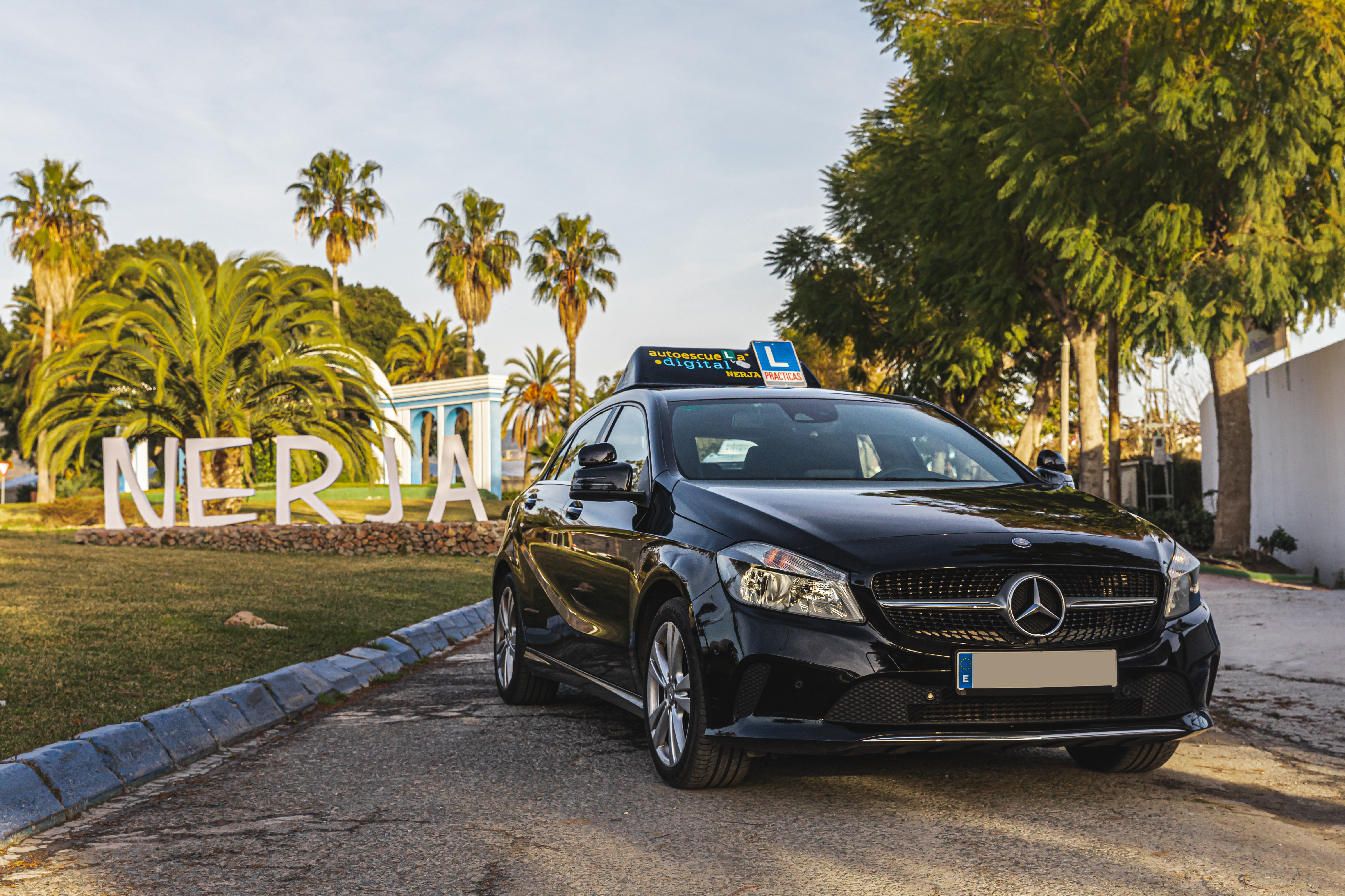 Mercedes con cartel Autoescuela Digital frente al letrero de Nerja